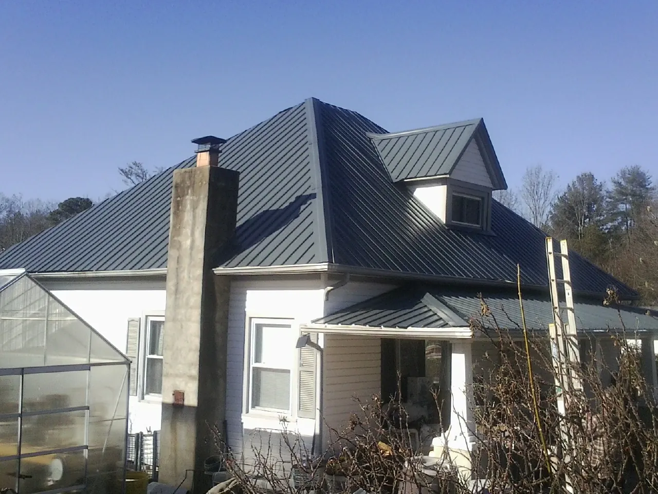 Dark blue standing seam metal roof on a white farmhouse with dormer — Slate & Tile Roof Repair by Roofing Brothers in Teasdale