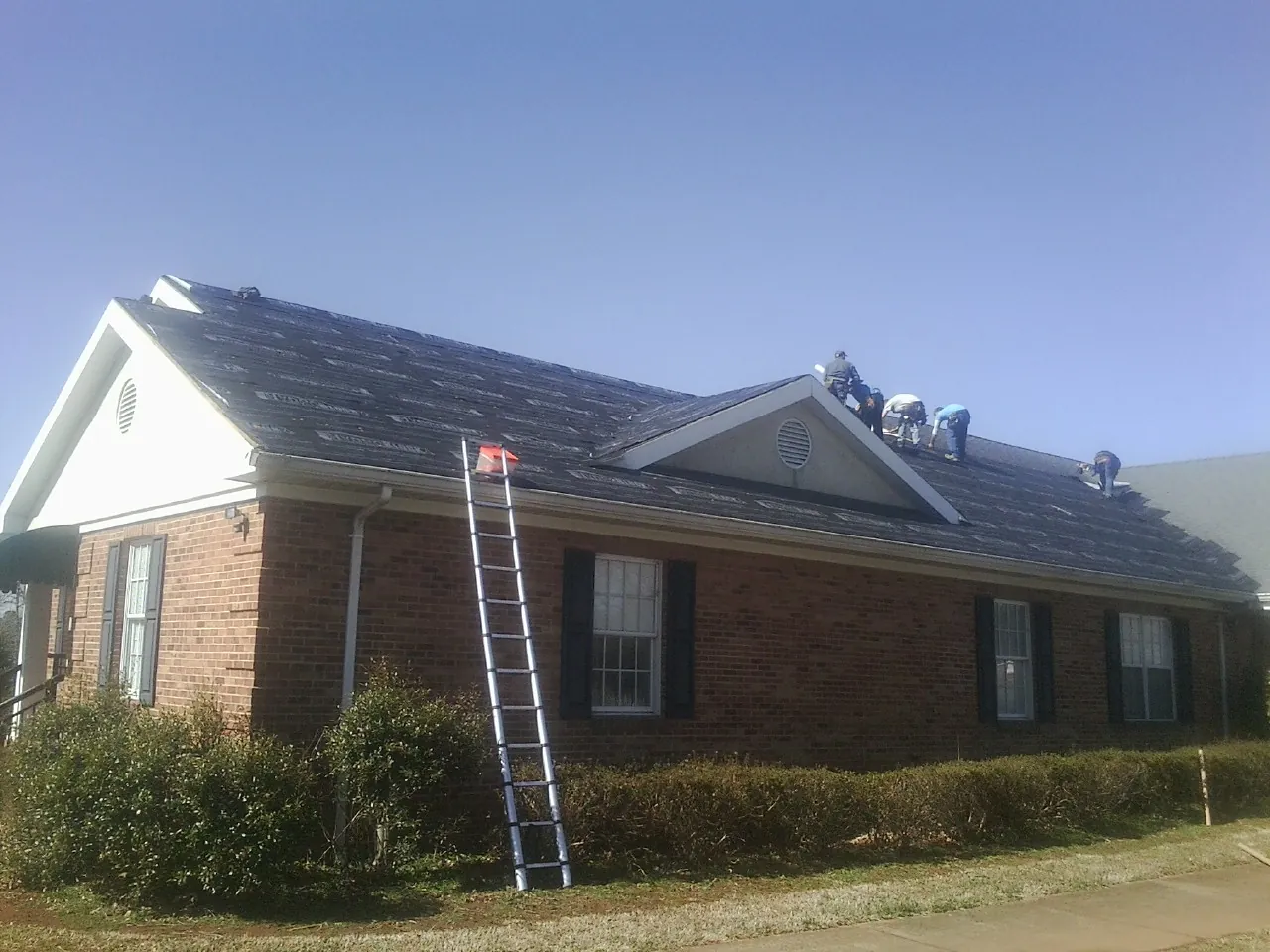 Crew tearing shingles off a brick ranch roof with a ladder set — Metal Roof Repair work by our crew in Teasdale