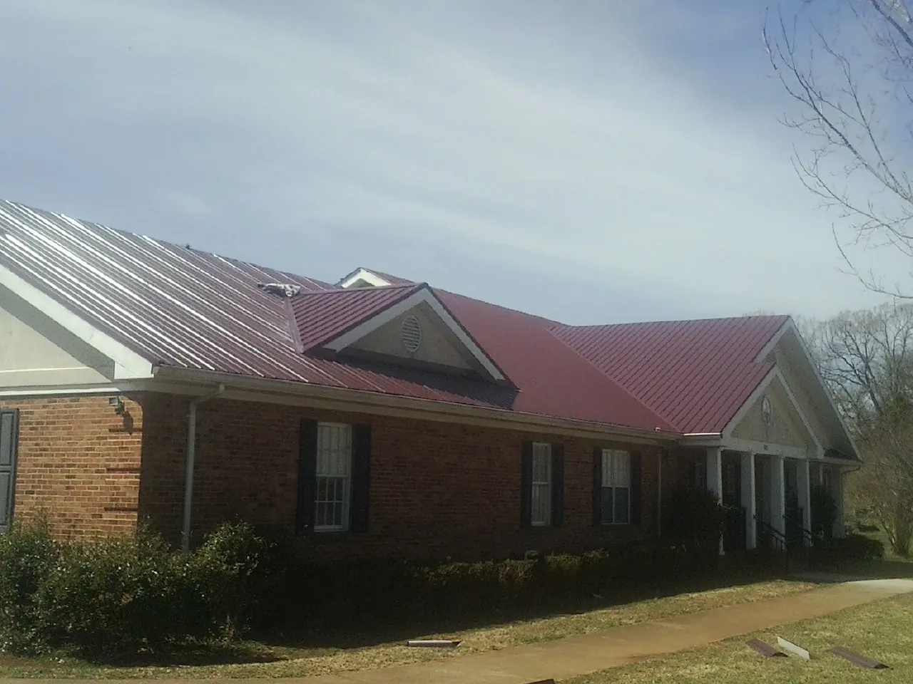 Red metal roof with gabled entries on a long brick building, from a Hail Damage Roof Repair job in Teasdale