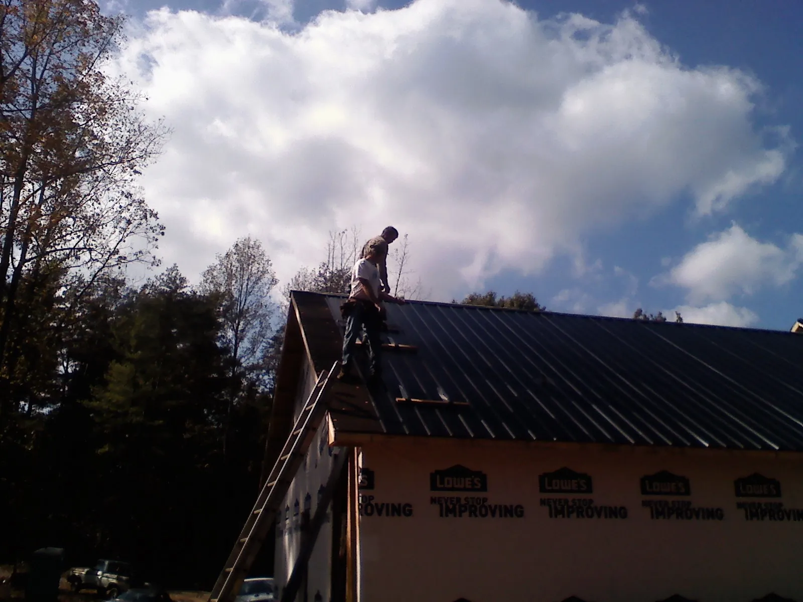Roofer fastening dark metal panels high against a cloudy sky, from a Roof Inspection job in Teasdale