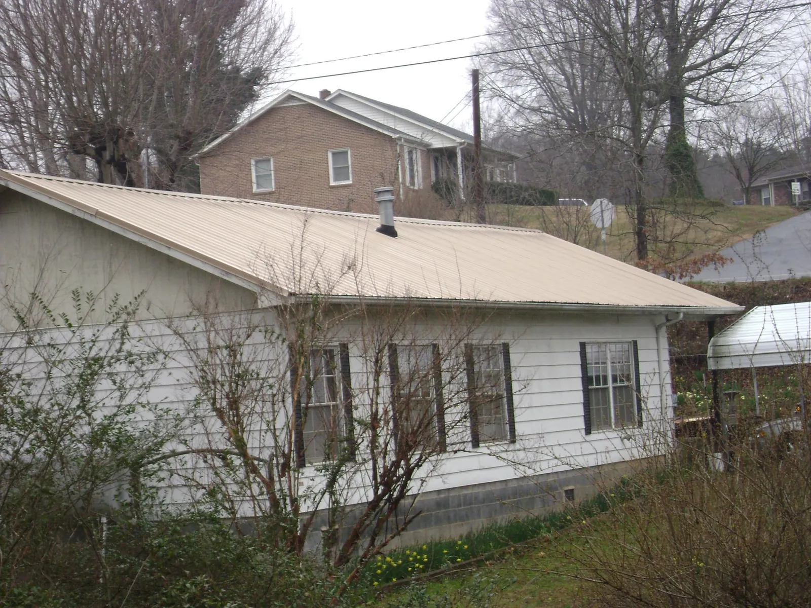 Tan metal roof on a white sided house set into a hillside — Commercial Roofing by Roofing Brothers in Teasdale